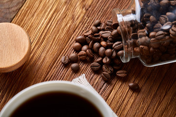 Roasted coffee beans get out of overturned glass jar on wooden background, selective focus, side view