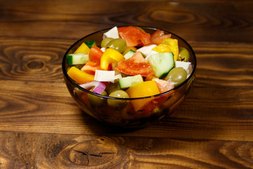 Greek salad in glass bowl on wooden table