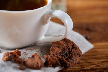 Morning coffee in white cup, chocolate chips cookies on homespun napkin, close-up, selective focus