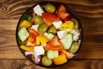 Greek salad in glass bowl on wooden table