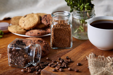 Conceptual composition with two jars of coffee beans, instant coffee and tasty cookies on wooden table, selective focus