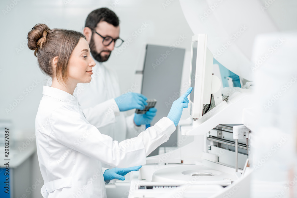 Wall mural Laboratory assistants in unifrom working with professional medical analizer at the laboratory