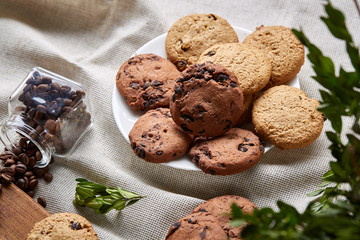 Side view of a plate of chocolate chip cookies on a white plate on homespun tablecloth, selective focus