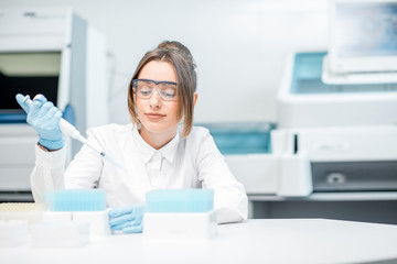 Young female laboratory assistant in uniform and protective glasses working with test tubes in the medical laboratory