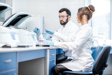 Laboratory assistants making analysis with test tubes and analyzer machines sitting at the modern laboratory