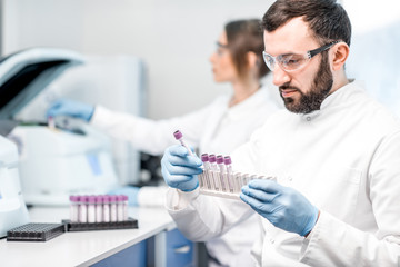 Male laboratory assistant making analysis with test tubes and analyzer machine sitting at the...