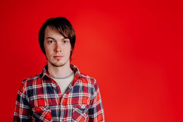 Portrait of a man in a plaid shirt on a red background, a man without emotions, a copy of a space