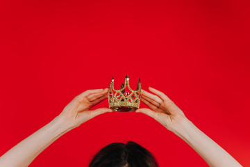 Golden crown on a red background in female hands over his head, she holds the crown over his head -...