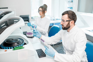 Laboratory assistants making analysis with test tubes and analyzer machines sitting at the modern...