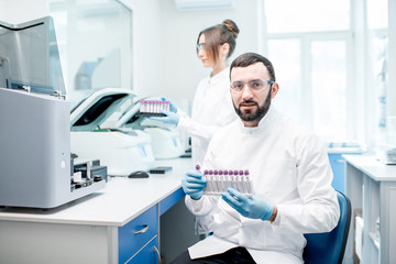 Portrait of a male laboratory assistant making analysis with test tubes and analyzer machines sitting at the modern laboratory