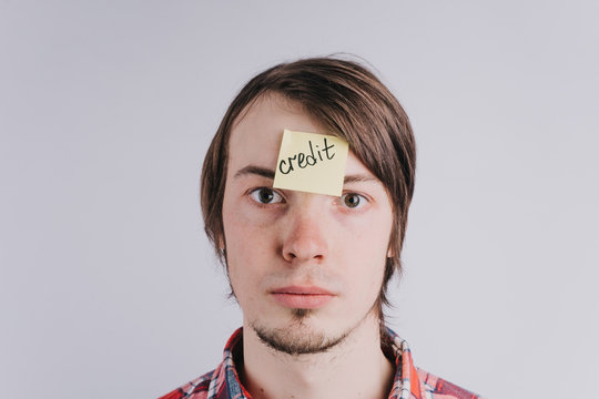 Sad man looks directly, a sticker on his forehead with the word credit. A young guy is upset by debt, credit. Close-up portrait, isolated
