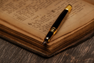old book and an ink pen on a wooden background.