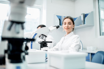 Young female medic in uniform working with microscope making analysis at the laboratory office