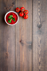 Tomato sauce in bowl with green basil near cherry tomatoes on dark wooden background top view copy space