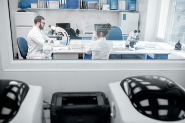 View through the window on the laboratory office with medics working with microscope