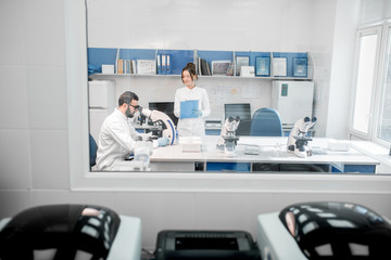 View through the window on the laboratory office with medics working with microscope