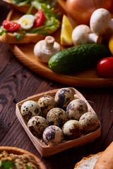 Fresh eggs of a quail with greens and vegetables on wooden table, selective focus, close-up