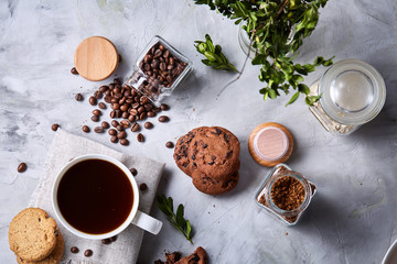 Coffee cup, jar with coffee beans, cookies over white background, selective focus, close-up, top view
