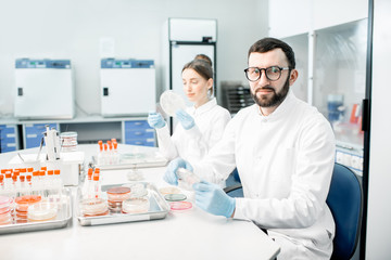 Portrait of a man in medical uniform during the bacteriological tests sitting with assistant in the modern laboratory