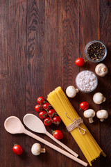 Uncooked pasta, tomatoes and spice on wooden background, top view, close-up, selective focus