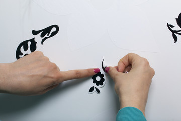 The girl glues the cut out elements from self-adhesive paper, to mask the defects of the white door.