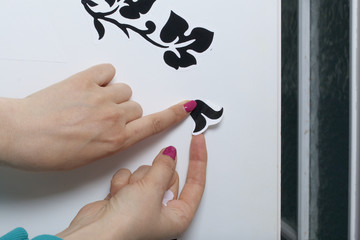 The girl glues the cut out elements from self-adhesive paper, to mask the defects of the white door.