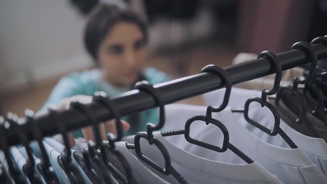 Woman choise clothes in shop, focus on hangers