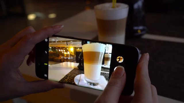 Girl makes a photo of a latte on a smartphone in a cafe close up