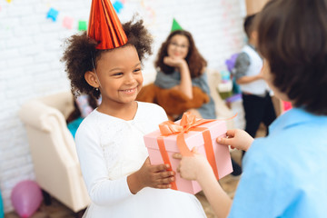 Joyful little girl in birthday hat waits for her to receive gift box. Gift time.