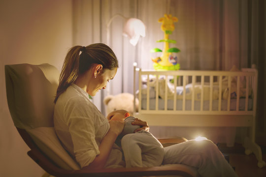 Young Beautiful Mother, Breastfeeding Her Newborn Baby Boy At Night, Dim Light