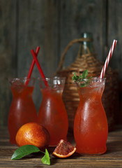 Close-up of three glasses with fresh home-made juice of a bloody orange with ice and mint on a vintage wooden background. Shallow depth of field, selective focus