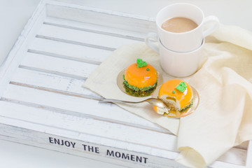 Bright orange mousse cakes and cup of coffee on white wooden tray