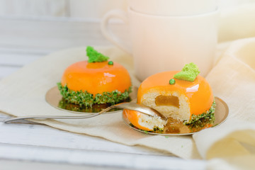 Bright orange mousse cakes and cup of coffee on white wooden tray