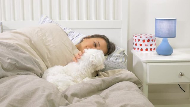Cute woman smiling to little dog in bed cuddling happy