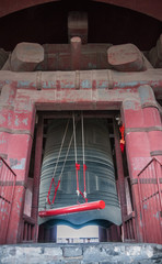 Beijing, China - April 26, 2010: Closeup of giant gray metal bell hanging from massive red support...