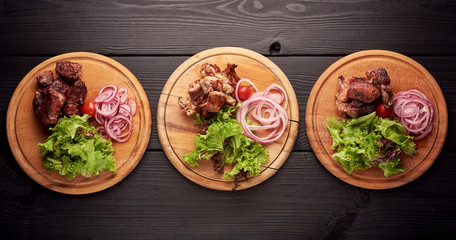 Different kinds of grilled meat as pork, chiken and beef on different plates with salad and vegetables. Kebab meat. Kebabs or meat skewerson black wooden background. copyspace