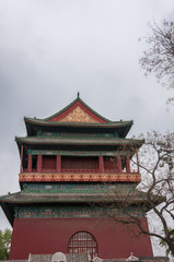 Beijing, China - April 26, 2010: Short side of upper structure of Drum Tower shows maroon, green and gold colors under gray sky. Some tree in photo.