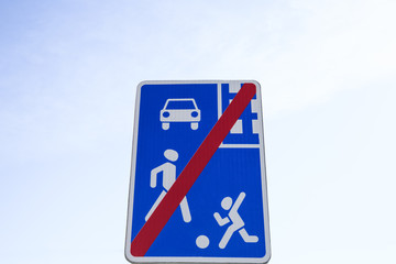 Traffic sign showing a car, a child and an adult. There is a thick red line crossing the sign diagonally. It`s a sign denoting the end of residential area with significant speed limits