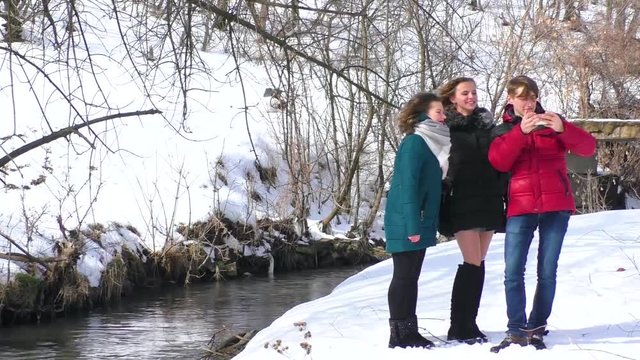 a company of friends play and make selfies by the river in winter