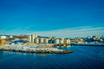 Outdoor view of industrial port area, showing ships and herring oil production plant during a winter season and blue sky, in port of Bodo, Norway