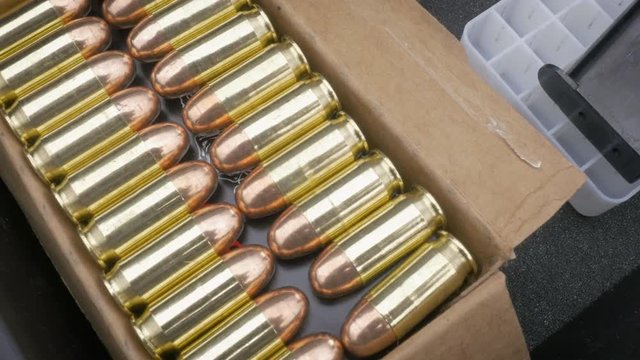 Push in towards a full box of 9mm bullets. The brass and copper ammunition sit in rows in a cardboard box. The ammo represents gun control and background checks for semi-automatic firearms.