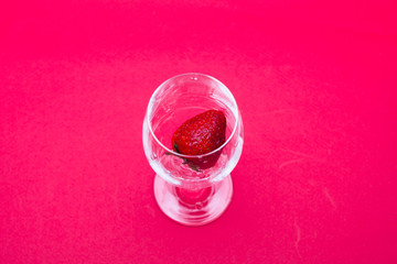 Ripe strawberries in a wine glass on red background