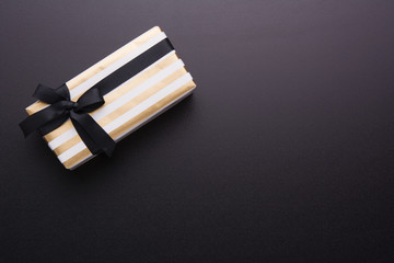 Hands holding wrapped gift box with colored ribbon as a present for Christmas, new year, mother's day, anniversary, birthday, party, on black background, top view. Present for a colleague at work.