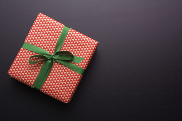 Hands holding wrapped gift box with colored ribbon as a present for Christmas, new year, mother's day, anniversary, birthday, party, on black background, top view. Present for a colleague at work.