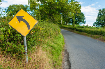 Yellow road sign on a rural road warning of a left-hand bend