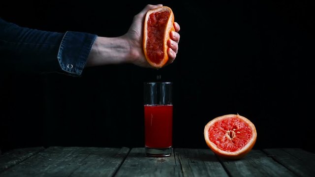 squeeze juice from grapefruit by hand on a black background. Cinemagraph.