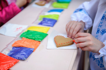 Child in embroidered shirt decorates gingerbread heart with red glaze
