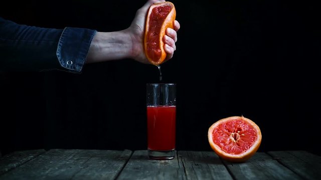 squeeze juice from grapefruit by hand on a black background