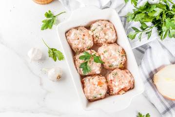 Raw homemade chicken or turkey meatballs in baking dish on white marble background. Copy space. top view