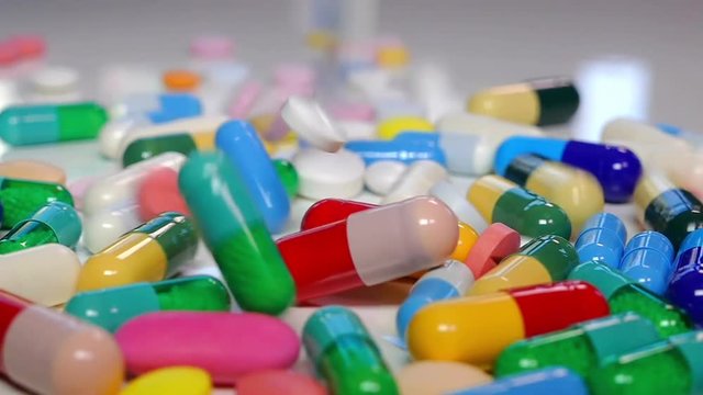Colorful drugs and pills falling on white table, concept of medical treatment, slow motion